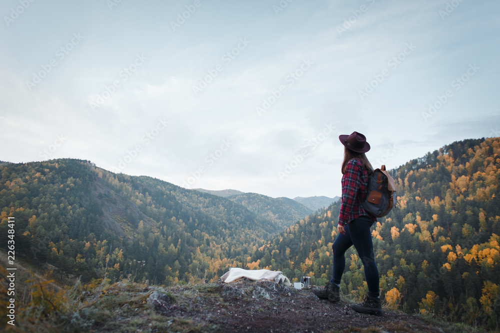 Young girl with backpack and hat view back on the background of autumn nature
