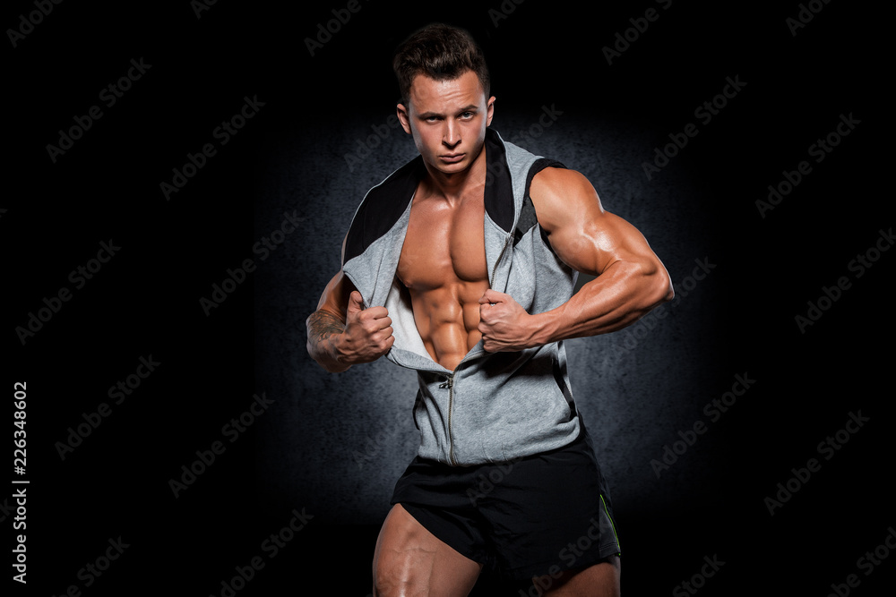 Young handsome athlete bodybuilder, in beautiful sportswear, demonstrates abdominals, against a dark background. Concept - power, beauty, biceps, triceps, sports equipment, gym, sports nutrition. Young handsome athlete bodybuilder, in beautiful sportswear, demonstrates abdominals, against a dark background. Concept - power, beauty, biceps, triceps, sports equipment, gym, sports nutrition.