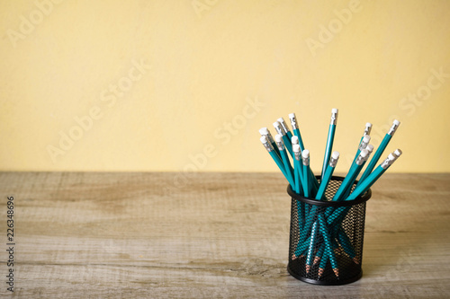  lead blue pencils in black metal holder pot on a yellow background