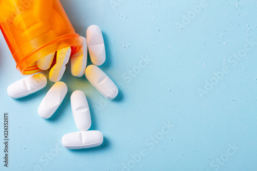 White pills in orange bottle on blue background close up with copy space photo