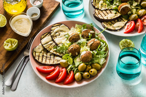 an appetizing dinner or lunch from a salad with tomatoes, grilled eggplants and legume falafel with sesame tahini dressing. Vegan healthy food for the whole family