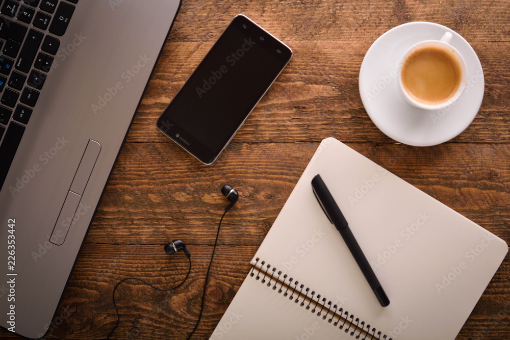 Cup of coffee on a laptop keyboard. Work place modern. Laptop (notebook) with cup of coffee and notepad with pen on old wooden table. Cup of coffee on a laptop keyboard. Work place modern. Laptop (notebook) with cup of coffee and notepad with pen on old wooden table.