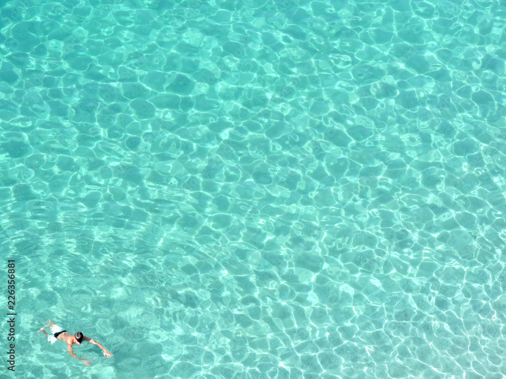 Boy swimming in a crystal clear water seen from above