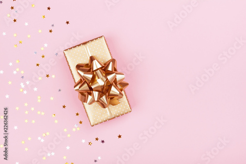 Golden gift or present box and stars confetti on pink background top view. Flat lay composition for birthday, christmas or wedding.