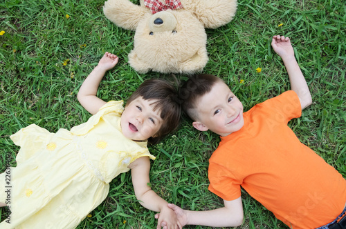 Top view of kids lying on the grass at park having fun. Little girl and boy relax with smiling. Teddy bear toy together photo