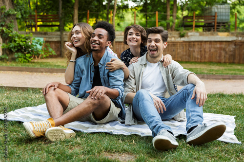 Young friends outdoors in park having fun sitting on grass.