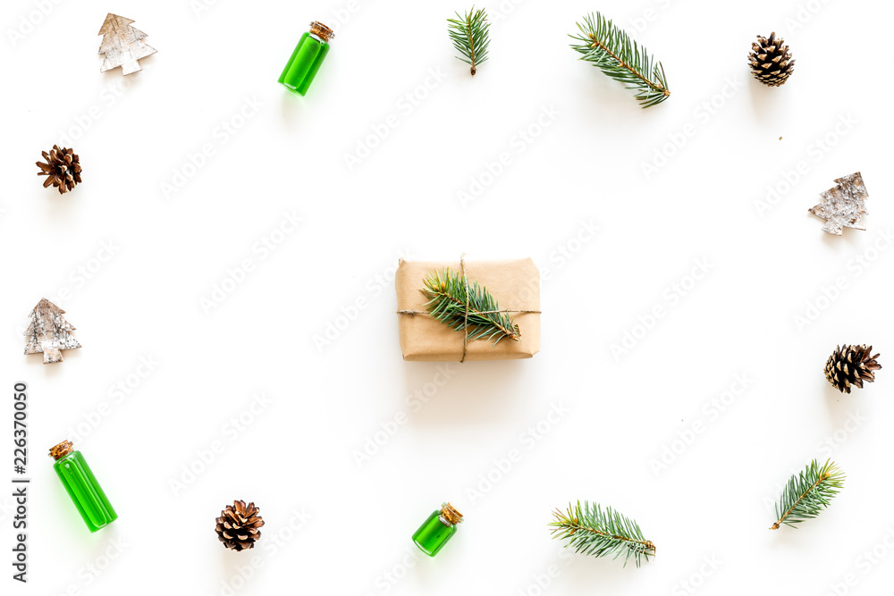New Year frame with pine sprigs, cones, spruce figure, fir oil and new year gift decorated with craft paper and pine sprout on white background top view copy space