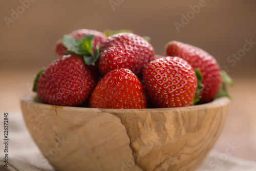 Ripe strawberries in wooden bowl on wood background