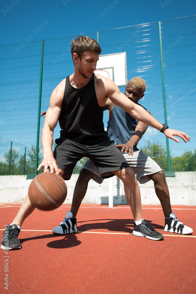 Naklejka premium Full length action shot of two muscular men playing basketball in outdoor court
