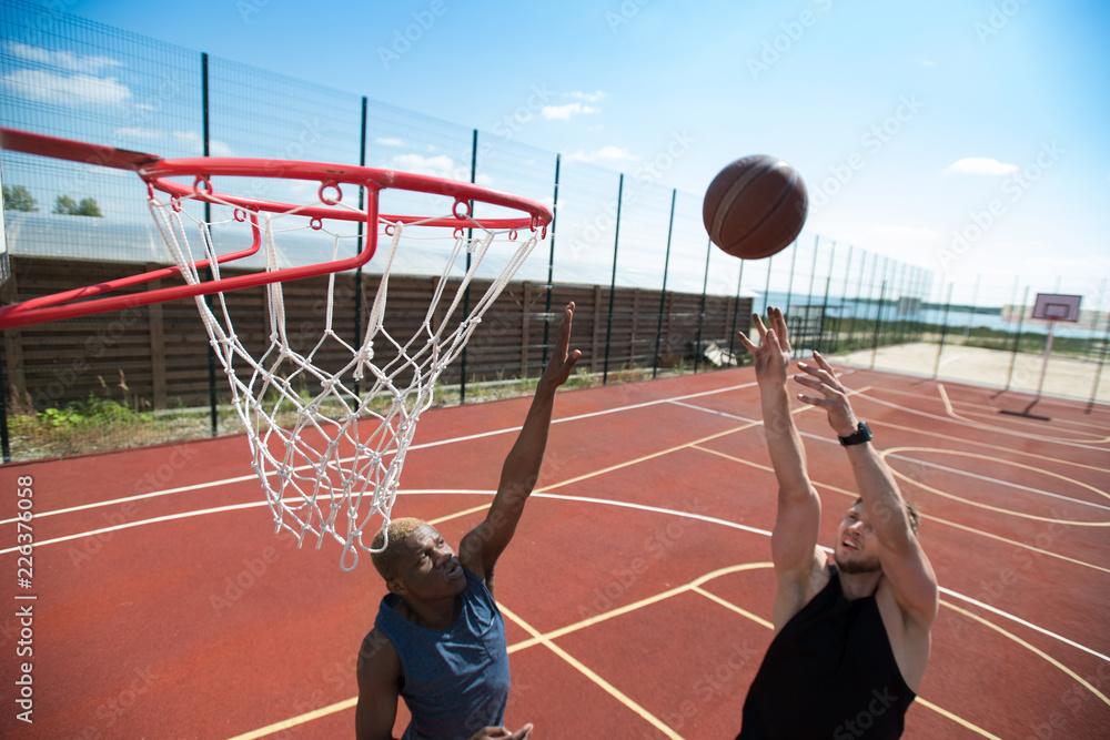 Naklejka premium Portrait of young basketball player throwing ball in basket on outdoor court lit by sunlight, copy space