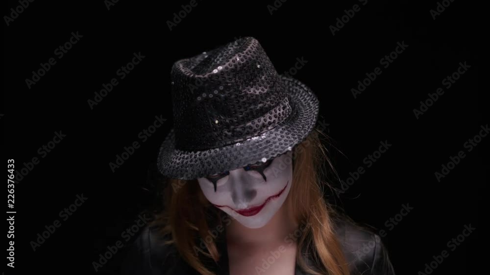 Girl clown standing on green background dressed in red dress and black hat showing finger on product confidently promoting product looking at camera smiling Girl clown standing on green background dressed in red dress and black hat showing finger on product confidently promoting product looking at camera smiling