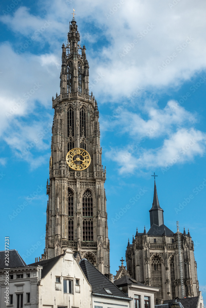 Antwerp, Belgium - September 24, 2018: Closeup of Towers of Onze-Lieve-Vrouwe Cathedral of Our Lady in back under blue cloudy sky. Parts of white facades up front.