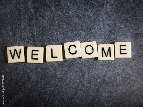 Letter tiles on black slate background spelling Welcome