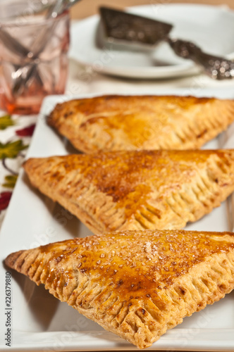 Front, top view, medium distance of three, freshly baked, homemade, cherry  cream turnovers , cooling on a white, rectangular plate, with a silver pie wedge 