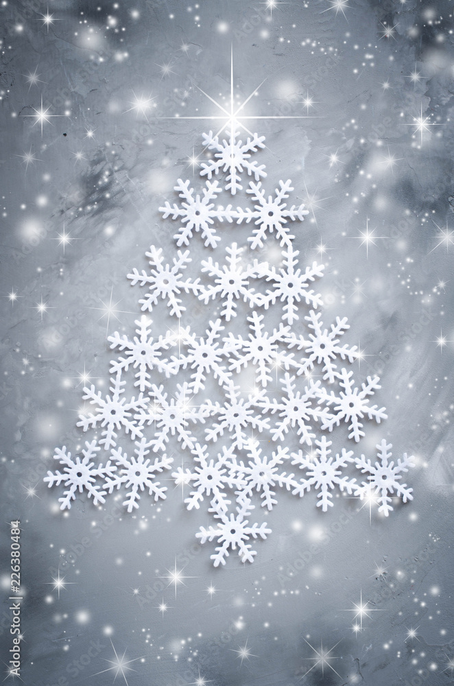 Decorative snowflakers laid in the form of a Christmas tree on a gray background.