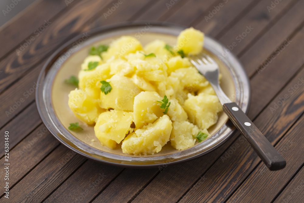 Boiled potatoes with fresh herbs and oil in a bowl on a wooden table