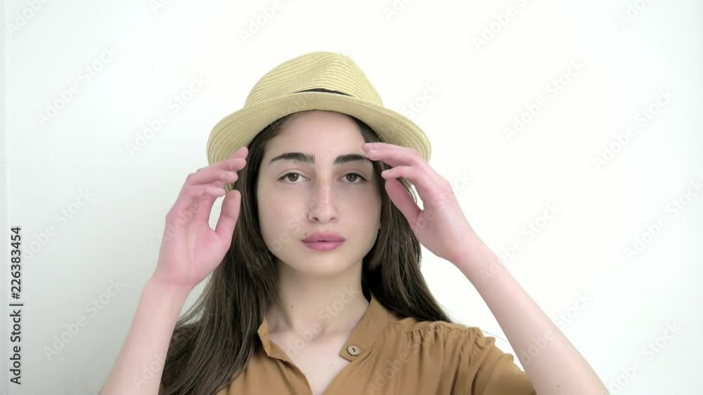 Attractive young woman in the hat looking to the camera and corrects hairstyles on the white background. Close up. Portrait shot Attractive young woman in the hat looking to the camera and corrects hairstyles on the white background. Close up. Portrait shot