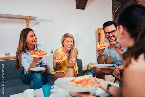 Group of friends laughing while eating pizza at home. photo
