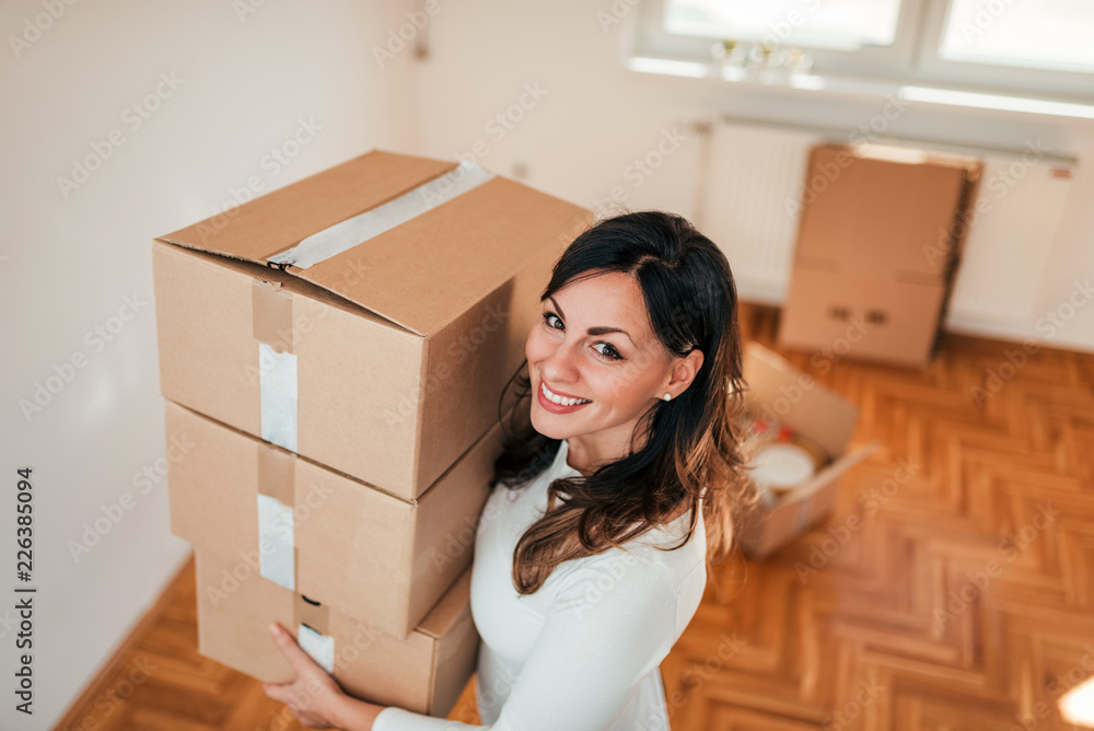 Smiling young woman holding cardboard boxes with belongings, looking at camera. Moving to a new apartment. Smiling young woman holding cardboard boxes with belongings, looking at camera. Moving to a new apartment.