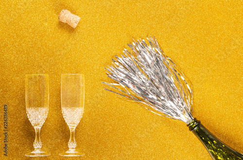 From above bottle with tinsel simulating Champagne with two galsses and cork on golden background photo