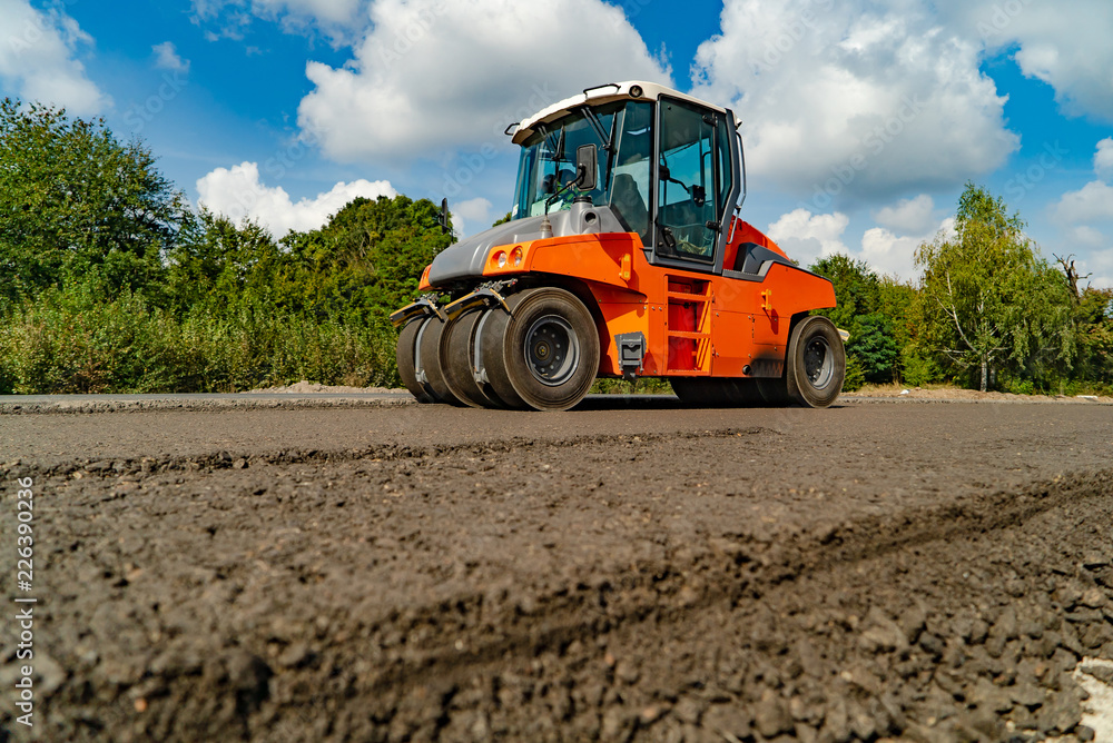 vibrating roller machine compacts asphalt using four hot wheels of rollers on the road. Close-up vibrating roller machine compacts asphalt using four hot wheels of rollers on the road. Close-up