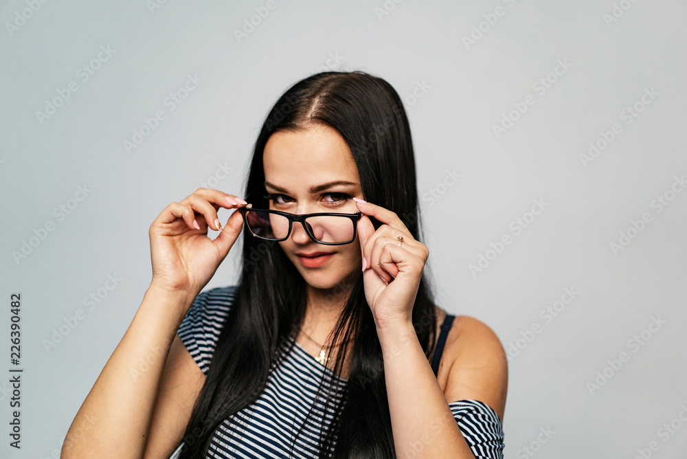beautiful model in striped clothes holds for temples of eyeglasses by both hands on a white background. Close-up beautiful model in striped clothes holds for temples of eyeglasses by both hands on a white background. Close-up