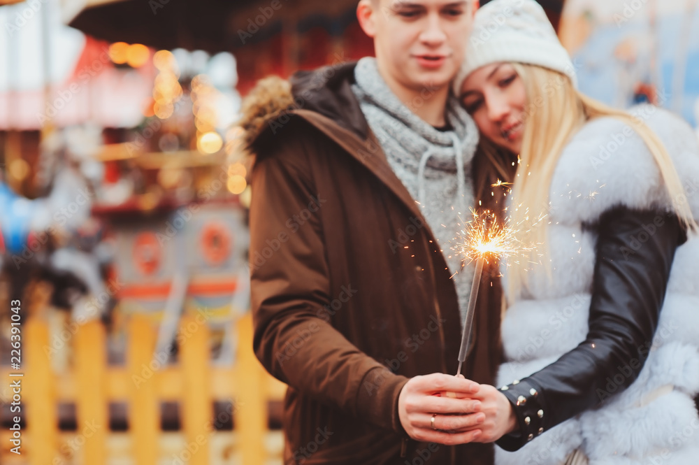 happy couple with christmas firelights walking in city holiday amusement park, carousel on background