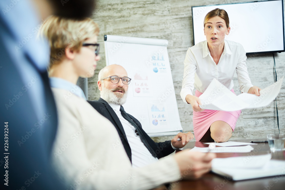 Irritated young businesswoman with one knee on table having argument with colleague at briefing Irritated young businesswoman with one knee on table having argument with colleague at briefing