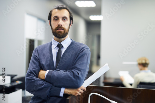 Young elegant serious businessman looking at camera while standing by tribune in conference hall or auditorium