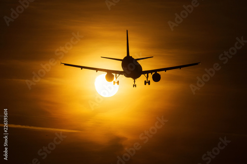 Silhouette of an air plane over the sun with beautiful red clouds in background