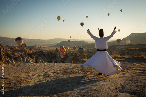 Dervish doing the retual in love valley of Cappadocia with balloons in background at sunrise. photo