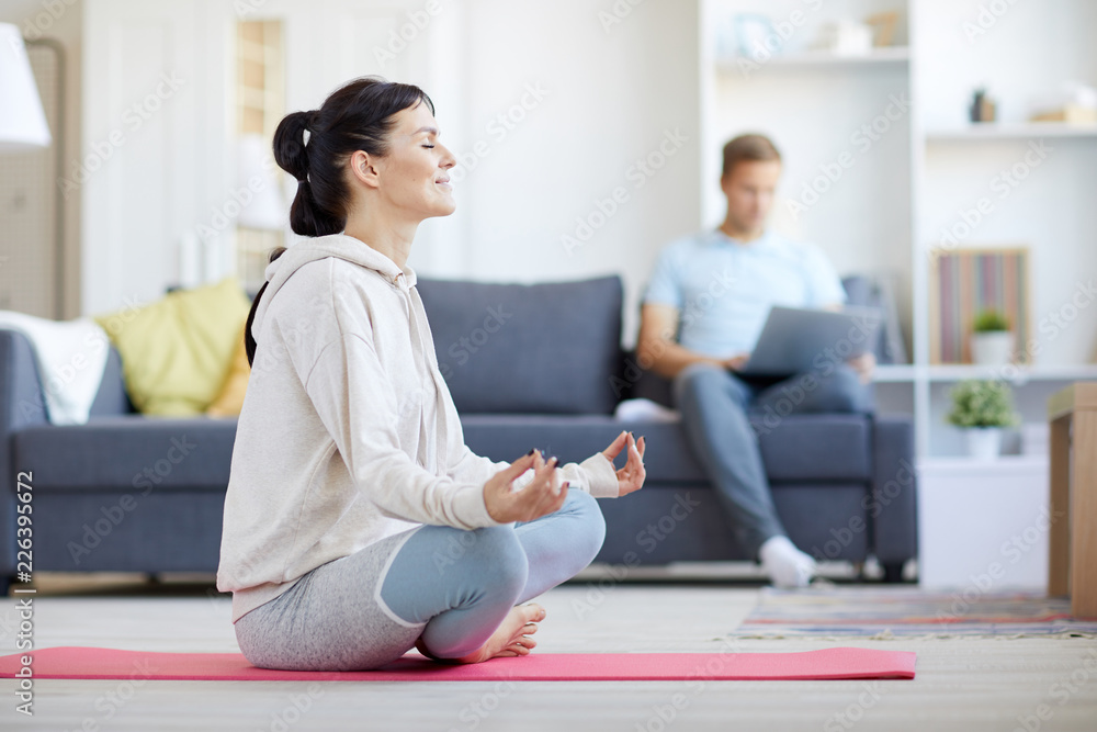 Young barefoot woman in activewear meditating in pose of lotus on the floor at home Young barefoot woman in activewear meditating in pose of lotus on the floor at home