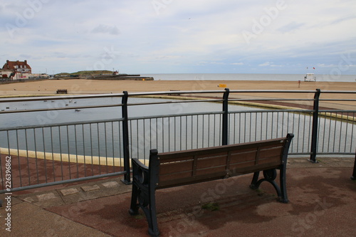 Tranquil sea view of of Art Deco bathing pond in Norfolk East Anglia view from empty bench of sandy beautiful beach  and ocean background tranquil scene with blue grey sky bench and life savers hut photo