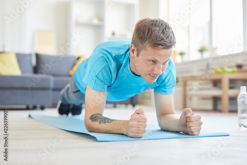 Young active man in blue t-shirt doing planks on the floor of living-room at home