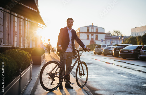 Handsome young man with his bicycle on the street in city center during sunrise