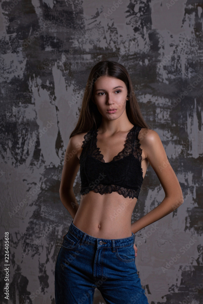 Test shoot of a pretty brunette girl posing in lace bra and blue jeans against grey wall