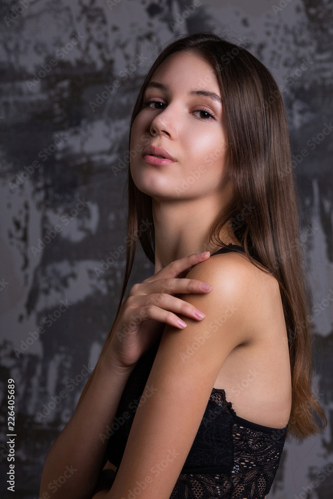 Fototapeta premium Test shoot of elegant brunette girl with perfect skin posing in a black lace bra against grey wall