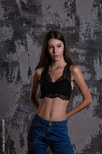 Test shoot of a pretty brunette girl posing in lace bra and blue jeans against grey wall