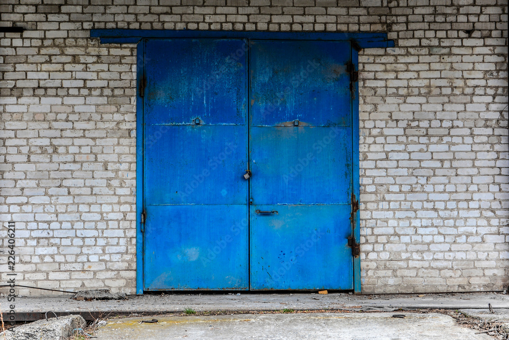 Iron gate, painted with blue paint and lock on the building of white brick. Warehouse, storage