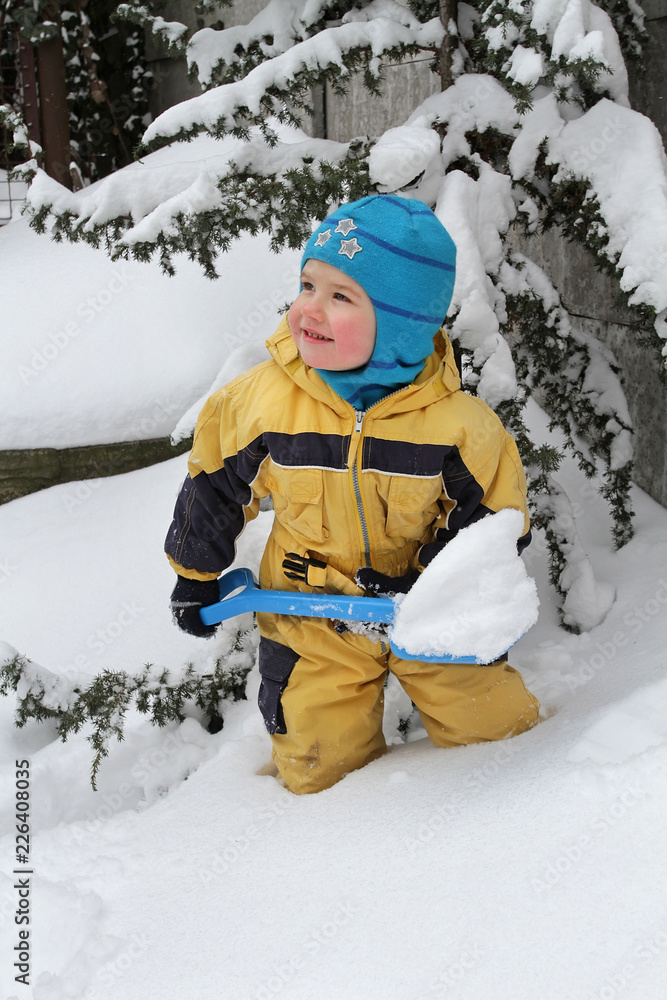 Fototapeta premium Little boy cleans snow with a toy shovel