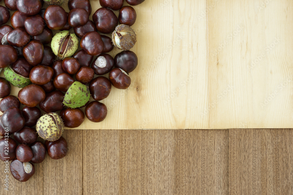 Simply autumn arrangement in brown colors, created from scattered chesnuts and wooden background with empty space for your text. Simply autumn arrangement in brown colors, created from scattered chesnuts and wooden background with empty space for your text.