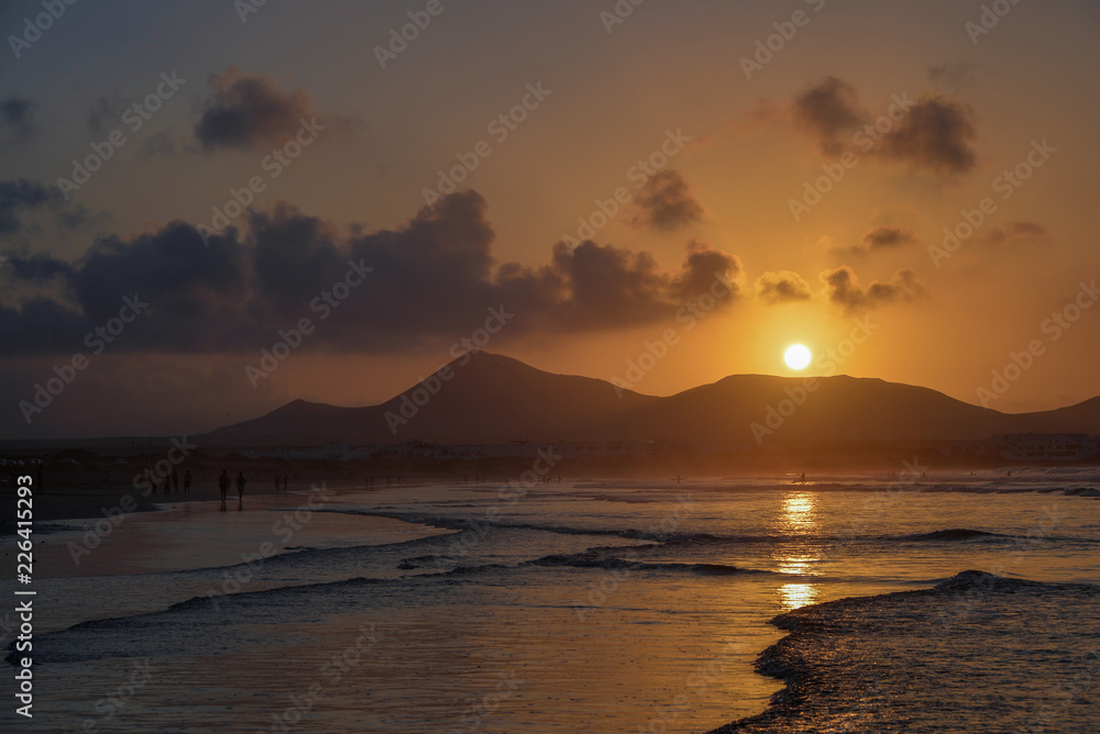 stunning sunset with a round sun over the volcanoes reflected in the low tide zone of the ocean