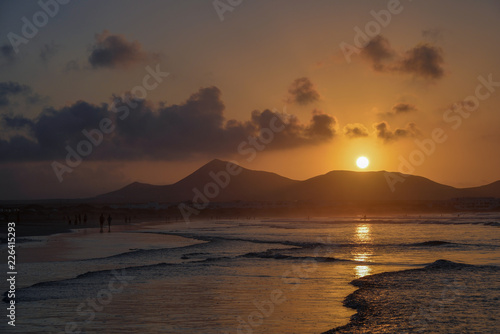 stunning sunset with a round sun over the volcanoes reflected in the low tide zone of the ocean