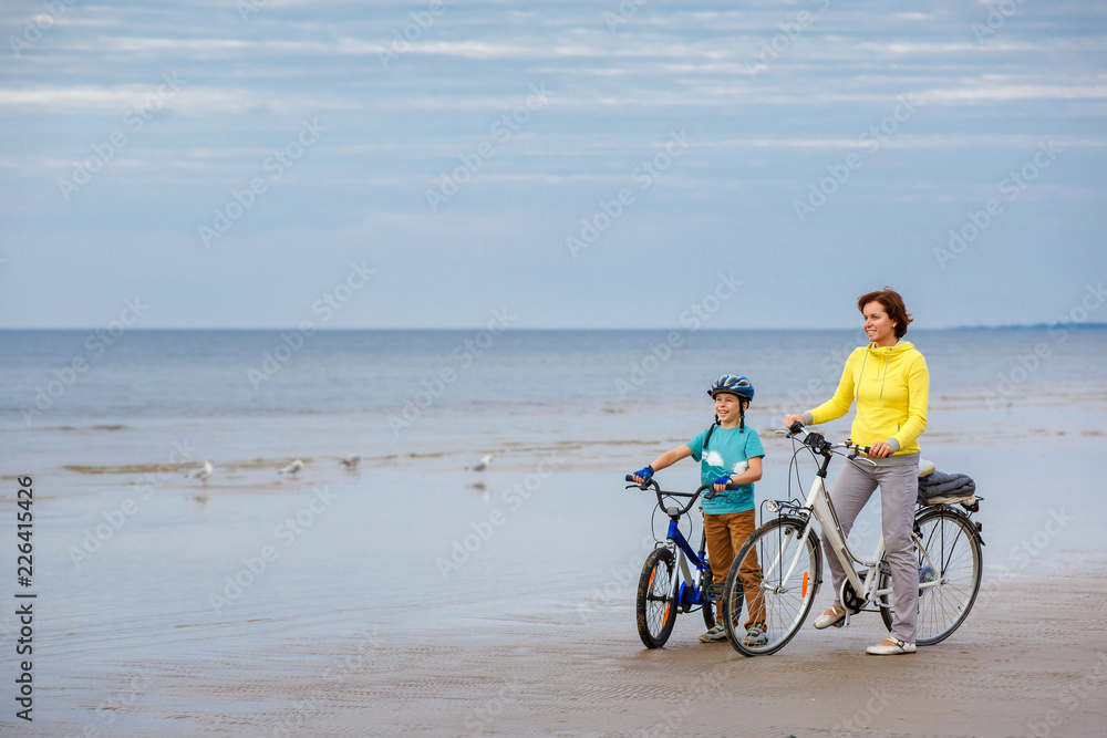 Fototapeta premium Young mother with her little son riding bicycles on beach