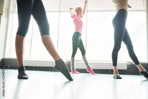 Side view low section of group of unrecognizable young women practicing ballet moves in sunlit dance studio, copy space