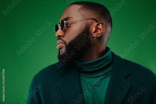 Man portrait. Style. Handsome Afro American guy in green jacket is looking away, on a green background