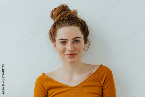 Woman portrait. Style. Beautiful blue eyed girl with freckles is looking at camera with a tender smile, on a white background