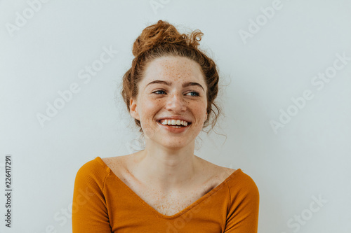 Woman portrait. Happiness. Beautiful blue eyed girl with freckles is looking away and laughing, on a white background