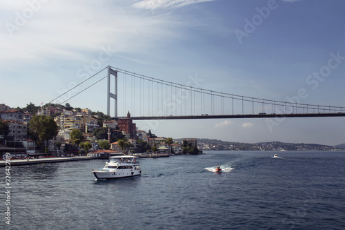 View of a white yacht, small boats, FSM bridge, Bosphorus and European side of Istanbul. It is a sunny summer day. © theendup