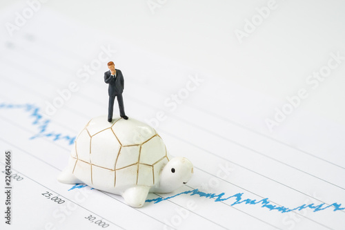 Invest with slow but steady for long term success metaphor, miniature people businessman riding turtle or tortoise walking on rising growth stock market value graph, value investment concept